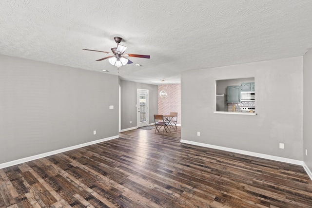 empty room with ceiling fan with notable chandelier, dark wood-type flooring, and a textured ceiling