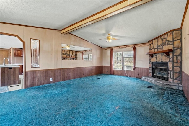 unfurnished living room with a stone fireplace, wood walls, lofted ceiling with beams, carpet floors, and a textured ceiling