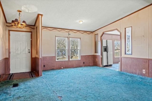 unfurnished living room with wood walls, crown molding, vaulted ceiling, a textured ceiling, and light colored carpet