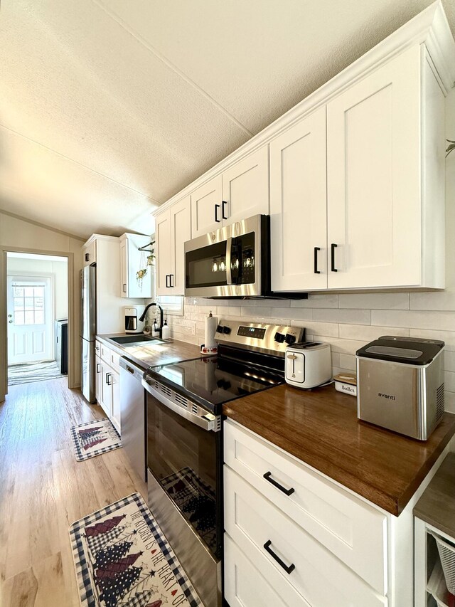 kitchen featuring wooden counters, appliances with stainless steel finishes, light wood-style floors, white cabinets, and a sink