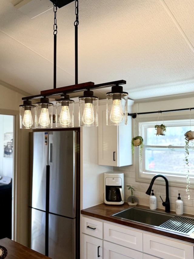 kitchen with a sink, white cabinetry, vaulted ceiling, backsplash, and freestanding refrigerator