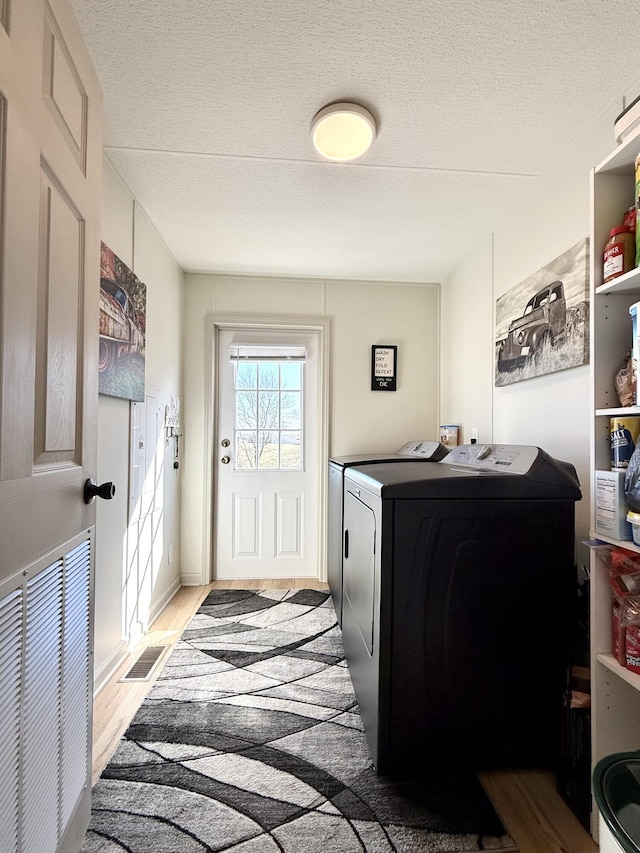 laundry room with visible vents, washing machine and dryer, a textured ceiling, light wood-type flooring, and laundry area