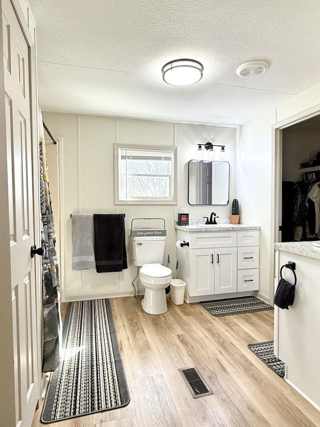 full bathroom with visible vents, toilet, vanity, a textured ceiling, and wood finished floors