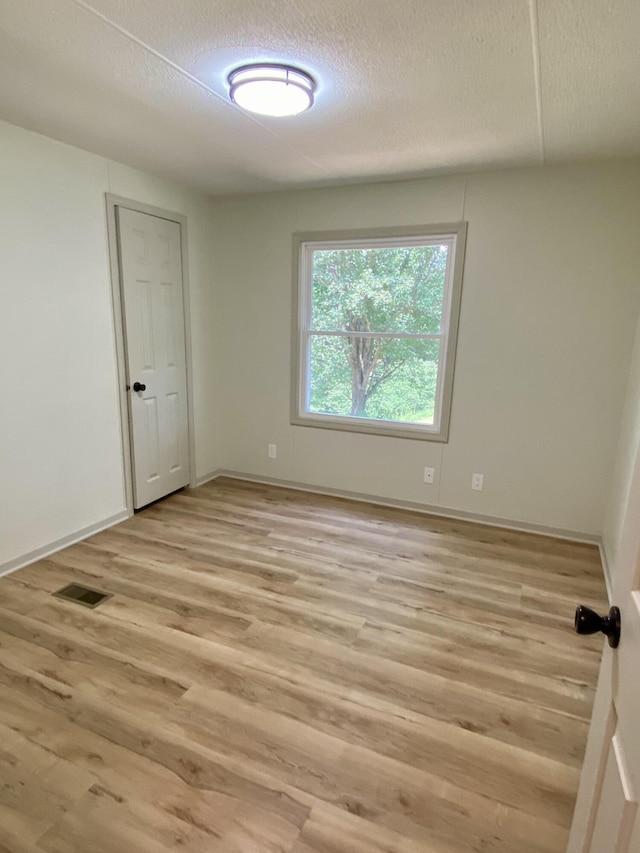 unfurnished room with a textured ceiling, light wood-style flooring, visible vents, and baseboards