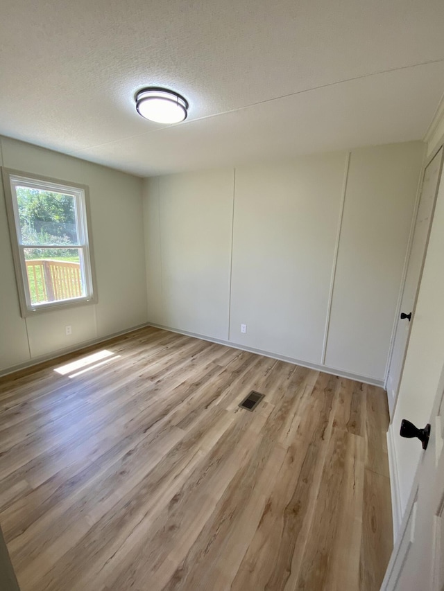 empty room with a textured ceiling, light wood finished floors, and visible vents