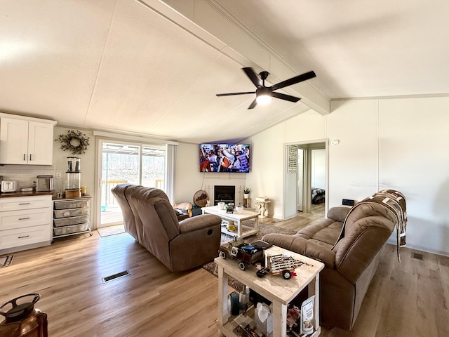 living area with a fireplace, visible vents, lofted ceiling with beams, ceiling fan, and light wood-type flooring