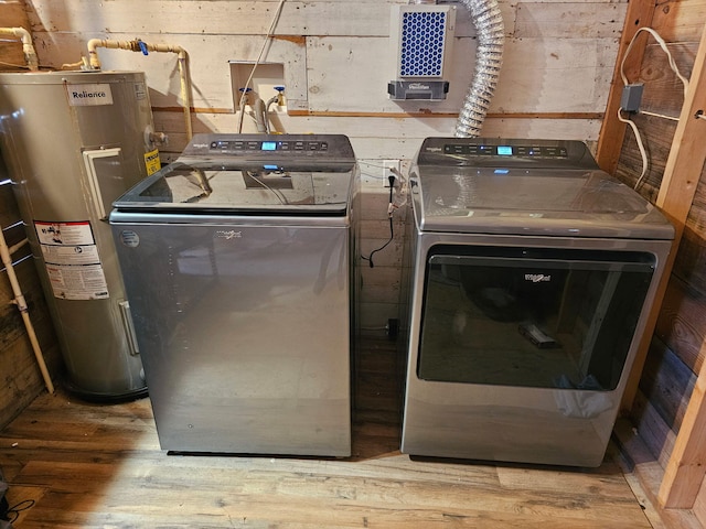 washroom with hardwood / wood-style floors, wooden walls, washing machine and dryer, and water heater