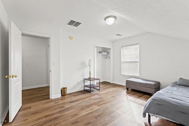 bedroom with lofted ceiling, hardwood / wood-style floors, and a textured ceiling