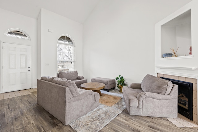 living room featuring a tiled fireplace, hardwood / wood-style floors, and high vaulted ceiling