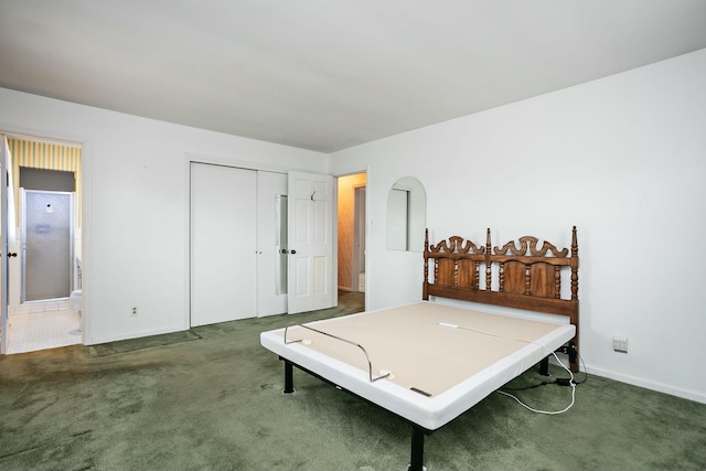 bedroom with ensuite bathroom, dark carpet, and a closet