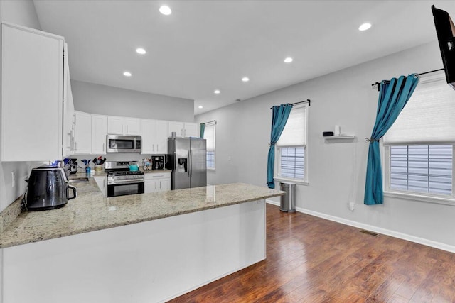 kitchen with dark wood-type flooring, light stone counters, appliances with stainless steel finishes, kitchen peninsula, and white cabinets