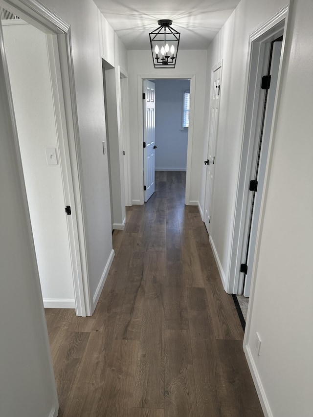 hallway with dark wood-type flooring and a chandelier