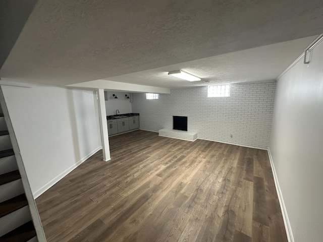 basement featuring brick wall, a textured ceiling, and dark hardwood / wood-style flooring