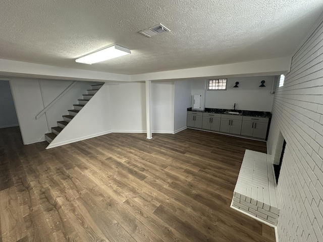 basement with a brick fireplace, sink, a textured ceiling, and dark hardwood / wood-style flooring