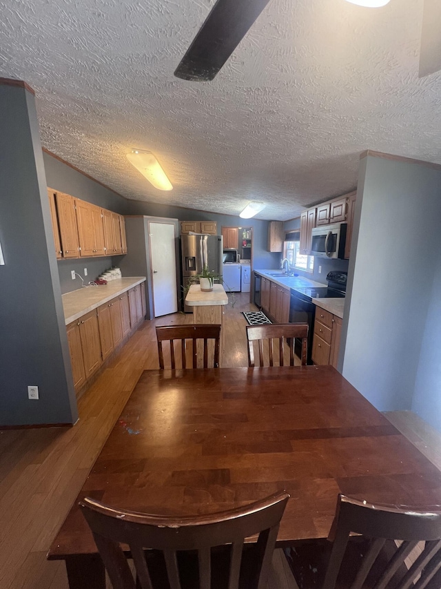 dining space featuring sink, a textured ceiling, independent washer and dryer, and light hardwood / wood-style flooring