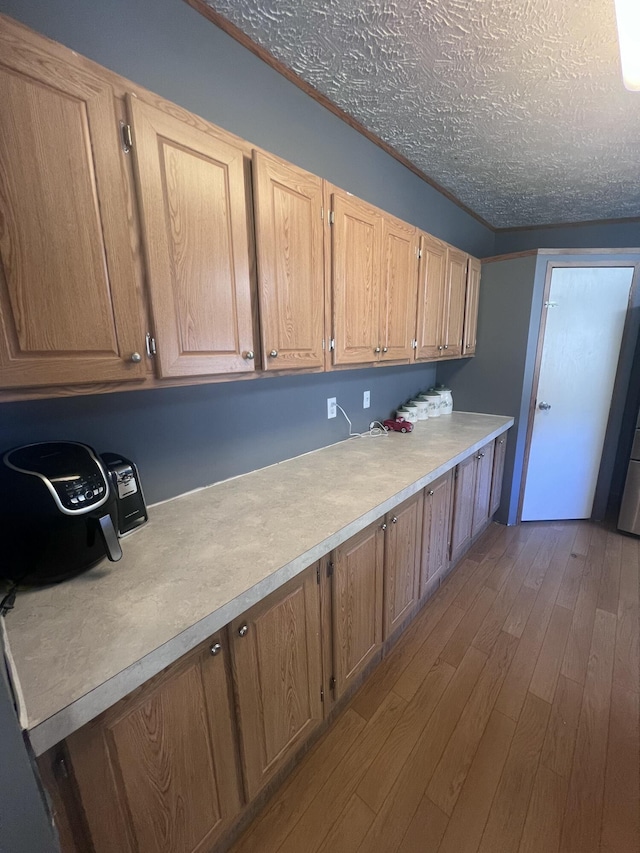 kitchen with crown molding, a textured ceiling, and light wood-type flooring