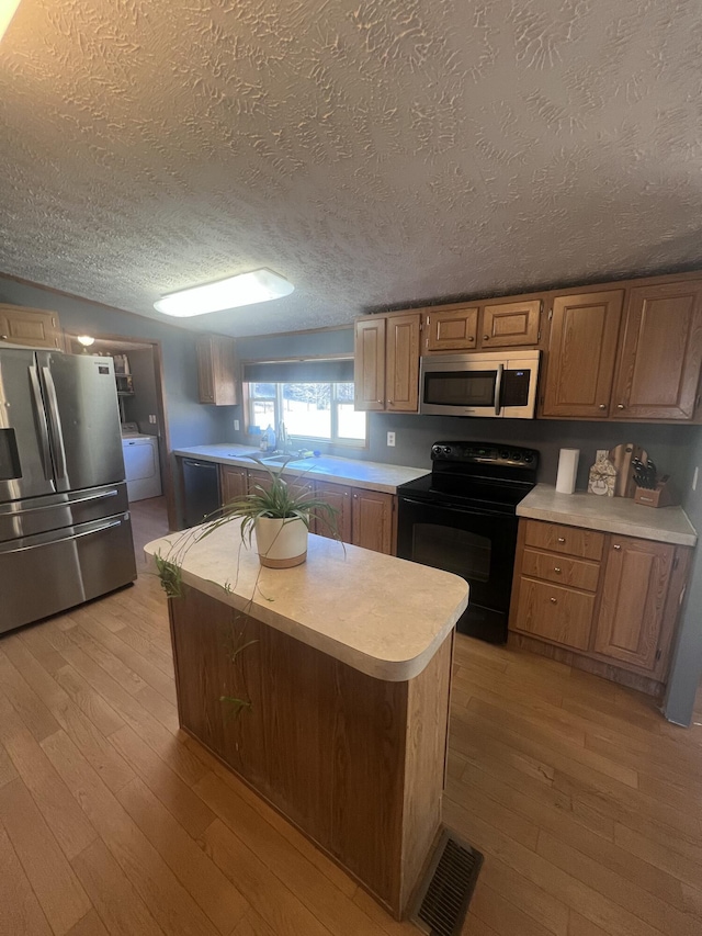 kitchen featuring light hardwood / wood-style flooring, black appliances, a textured ceiling, and a kitchen island