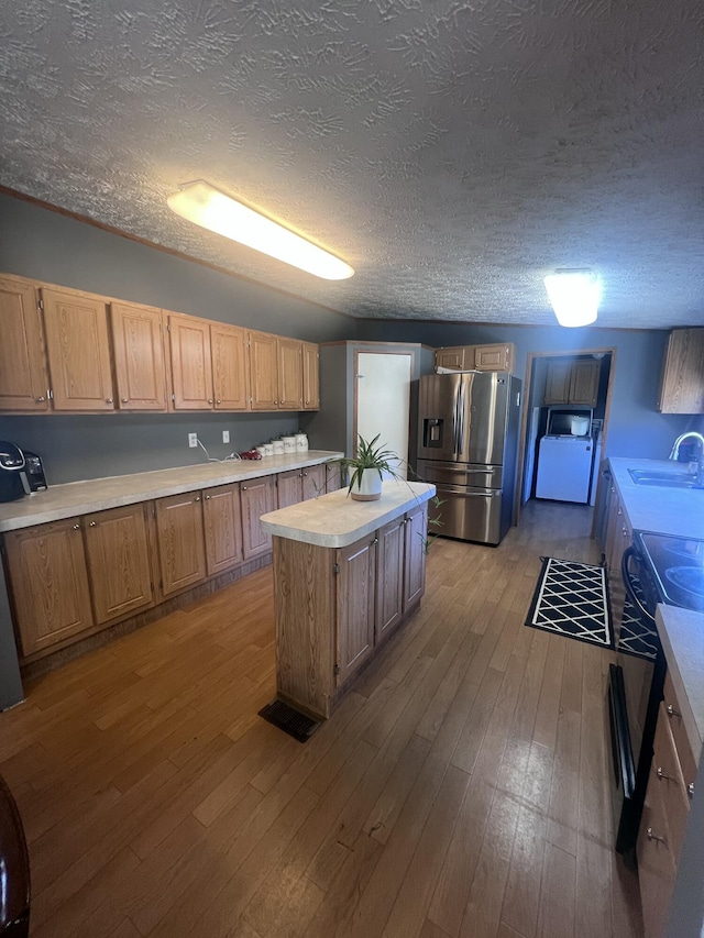 kitchen featuring sink, stainless steel refrigerator with ice dispenser, a textured ceiling, a kitchen island, and light wood-type flooring