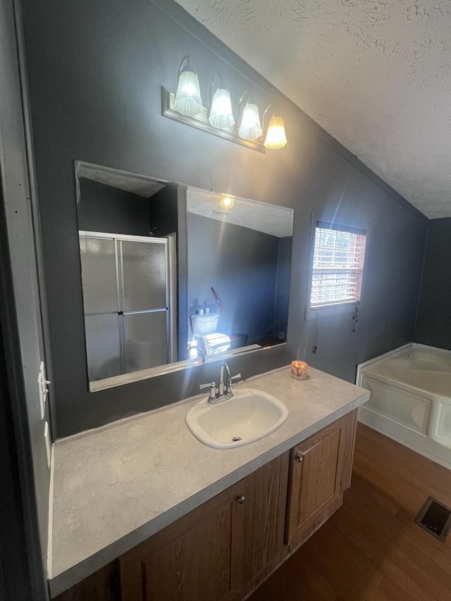 bathroom with vaulted ceiling, independent shower and bath, hardwood / wood-style flooring, vanity, and a textured ceiling