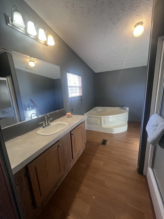 bathroom with vaulted ceiling, a bathing tub, hardwood / wood-style flooring, vanity, and a textured ceiling