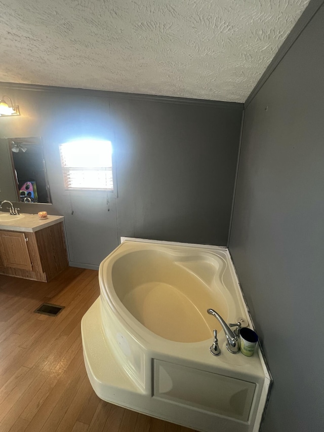 bathroom featuring crown molding, a textured ceiling, vanity, a tub, and hardwood / wood-style flooring