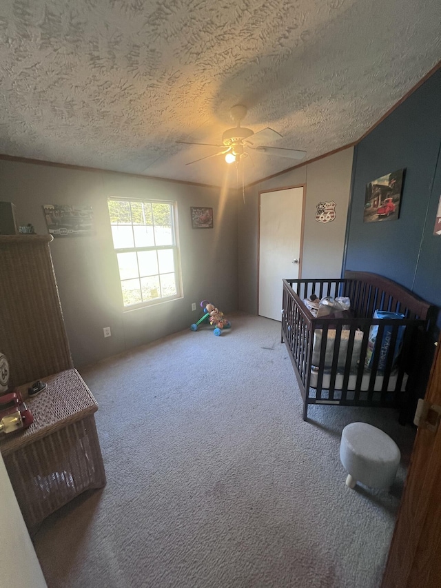 bedroom with a textured ceiling, ornamental molding, carpet flooring, a nursery area, and ceiling fan