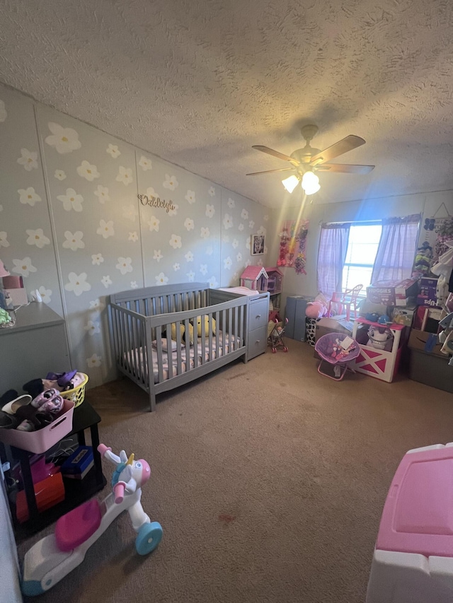 carpeted bedroom with a crib, a textured ceiling, and ceiling fan