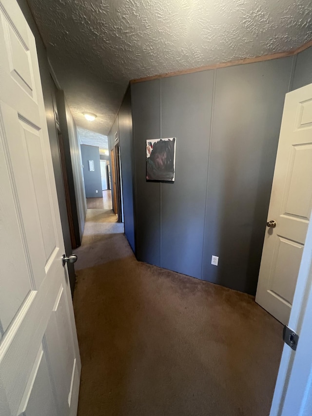 hall featuring a textured ceiling and dark carpet