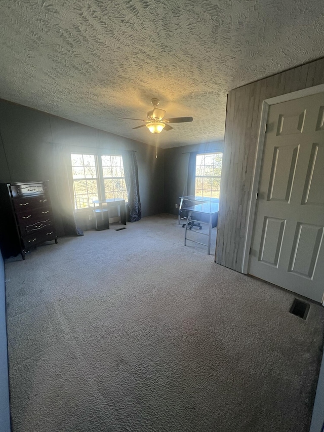 empty room featuring ceiling fan, carpet, a textured ceiling, vaulted ceiling, and wood walls