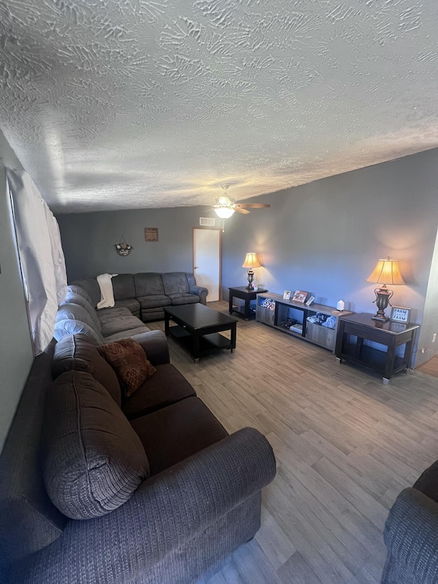 living room featuring wood-type flooring, ceiling fan, and a textured ceiling