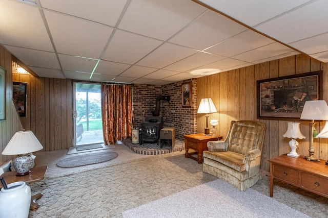 living area featuring carpet, a wood stove, a drop ceiling, and wood walls