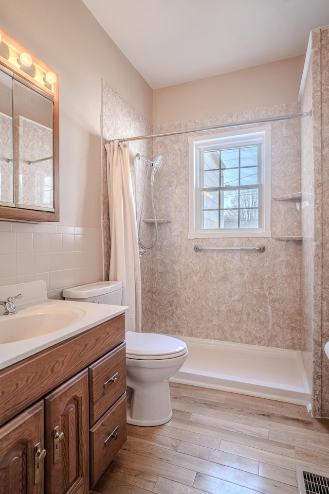 bathroom with tile walls, vanity, wood-type flooring, toilet, and walk in shower