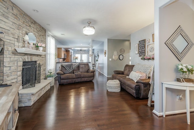 living room with a stone fireplace and dark wood-type flooring