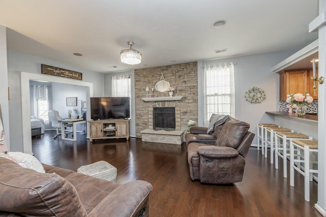 living room featuring a stone fireplace, dark hardwood / wood-style floors, and a healthy amount of sunlight