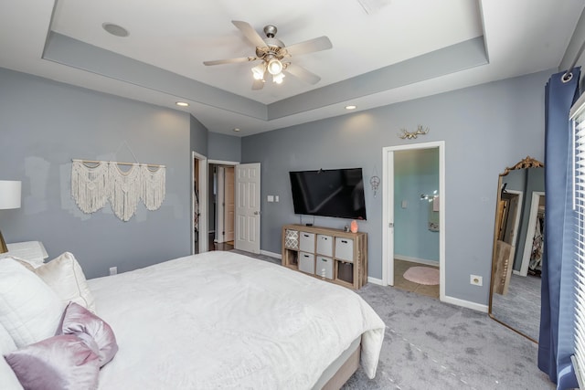 bedroom with a raised ceiling, connected bathroom, light colored carpet, and ceiling fan