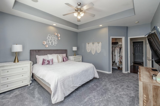 carpeted bedroom with ceiling fan, a walk in closet, a tray ceiling, and a closet