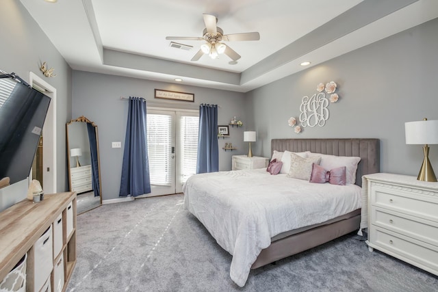 carpeted bedroom with ceiling fan, access to exterior, and a raised ceiling