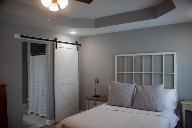 bedroom with ceiling fan, a barn door, and a raised ceiling