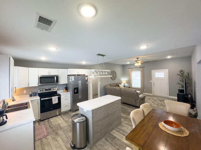 kitchen featuring sink, appliances with stainless steel finishes, light hardwood / wood-style floors, white cabinets, and decorative light fixtures