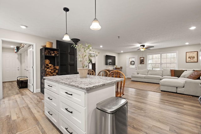 kitchen with a kitchen island, pendant lighting, white cabinets, light stone countertops, and light hardwood / wood-style flooring