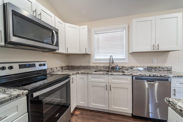 kitchen with vaulted ceiling, appliances with stainless steel finishes, white cabinetry, sink, and light stone counters