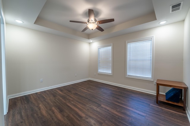 spare room with dark wood-type flooring, a raised ceiling, and ceiling fan