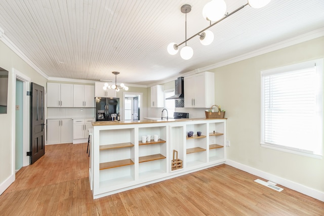 kitchen featuring pendant lighting, white cabinets, black refrigerator with ice dispenser, kitchen peninsula, and wall chimney exhaust hood