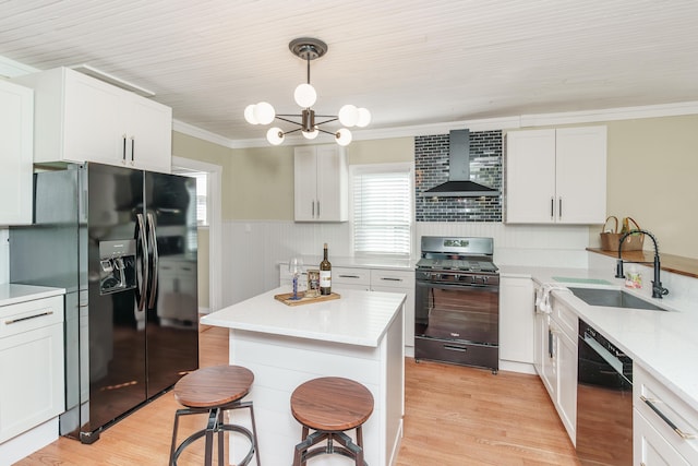 kitchen with pendant lighting, white cabinetry, sink, black appliances, and wall chimney exhaust hood