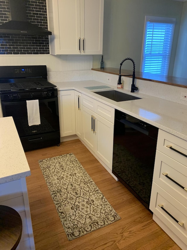 kitchen with white cabinets, wall chimney exhaust hood, sink, and black appliances