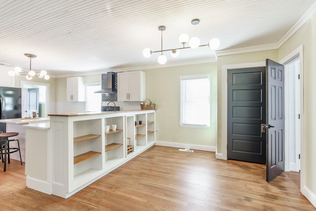 kitchen featuring wall chimney range hood, hanging light fixtures, white cabinets, a kitchen bar, and kitchen peninsula