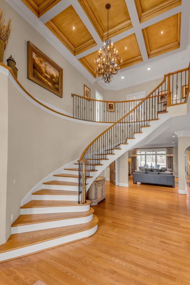 stairway featuring ornamental molding, a towering ceiling, hardwood / wood-style floors, and a notable chandelier