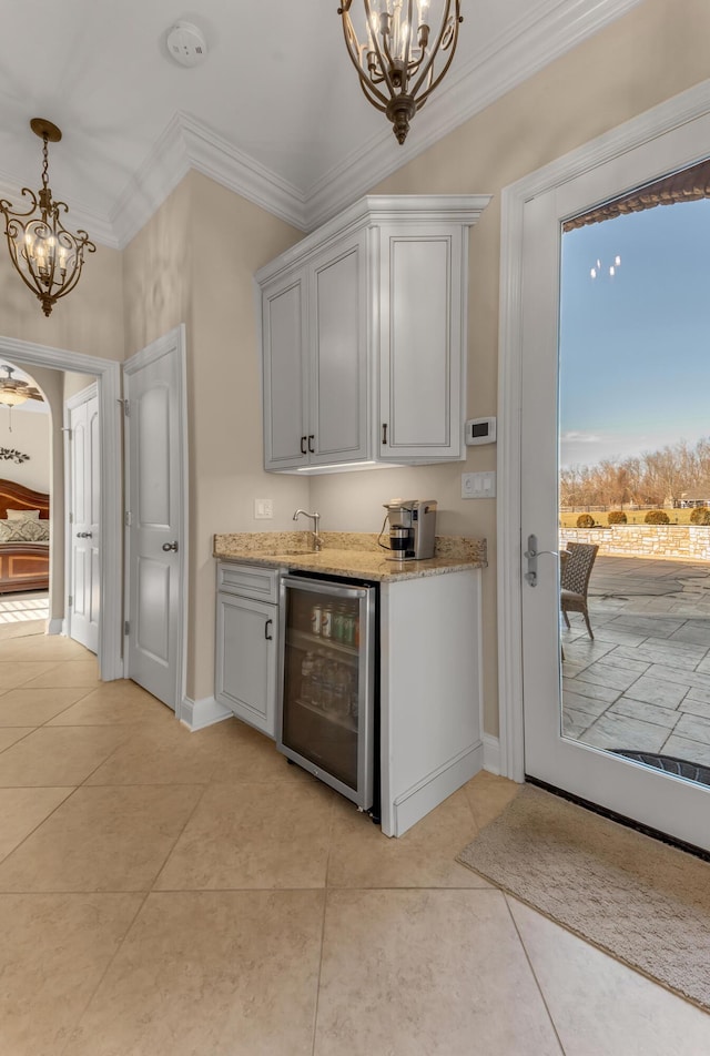 bar featuring a notable chandelier, ornamental molding, light tile patterned flooring, and beverage cooler