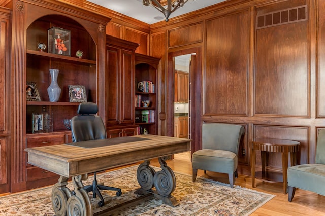 office with ornamental molding, light hardwood / wood-style flooring, wood walls, and built in shelves