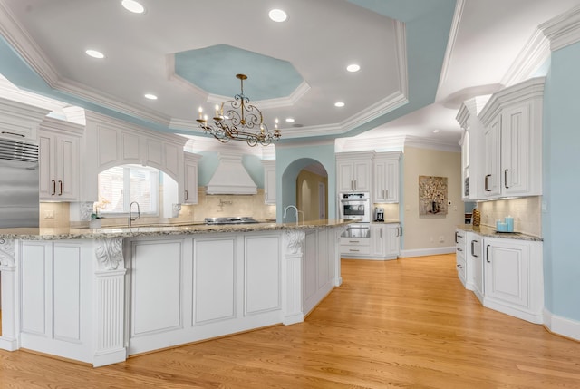 kitchen with decorative light fixtures, white cabinetry, custom exhaust hood, a tray ceiling, and stainless steel appliances